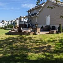 Outdoor seating area on a grassy hill; tables with umbrellas, stone retaining walls, buildings in the background.