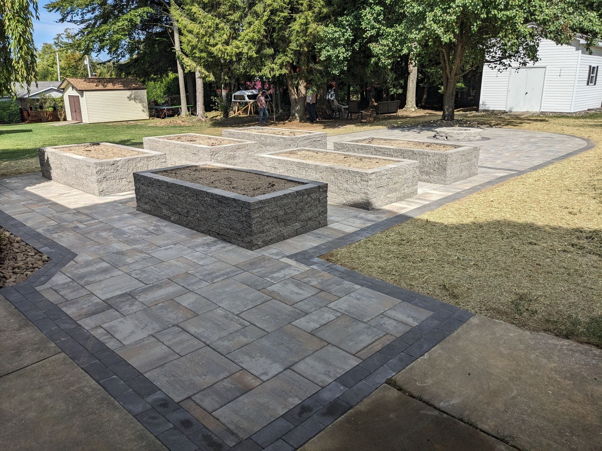 Black mulched hillside with plants and patio with furniture.