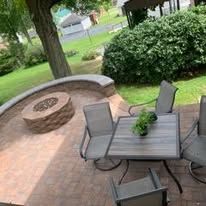 Patio with fire pit and seating, edged with gravel, beside a house and grassy area.