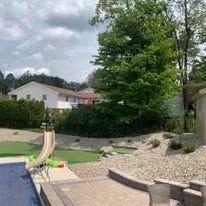 Stone steps and patio lead to a landscaped hillside with dark mulch and various green plants.