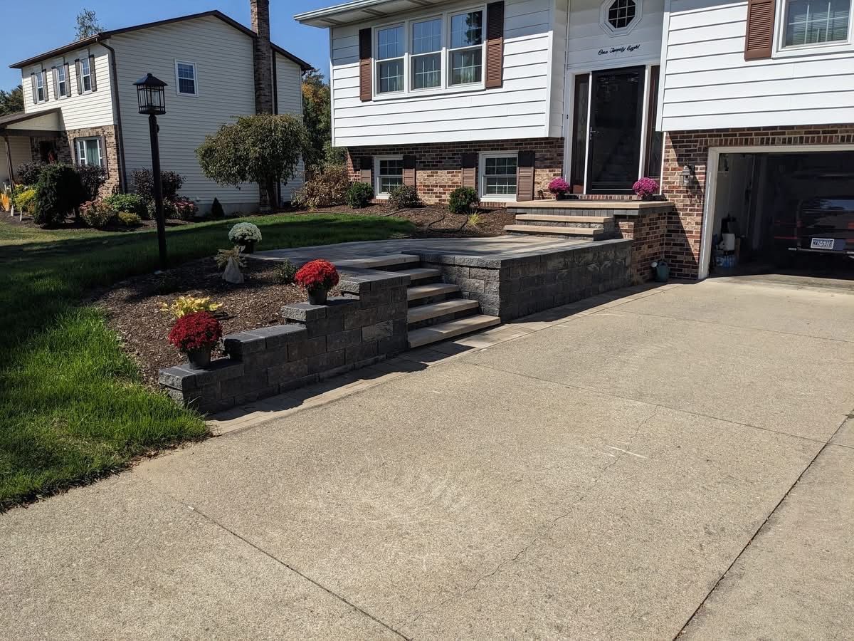 A house with a concrete driveway and retaining wall steps leading to the front door, with flowers.
