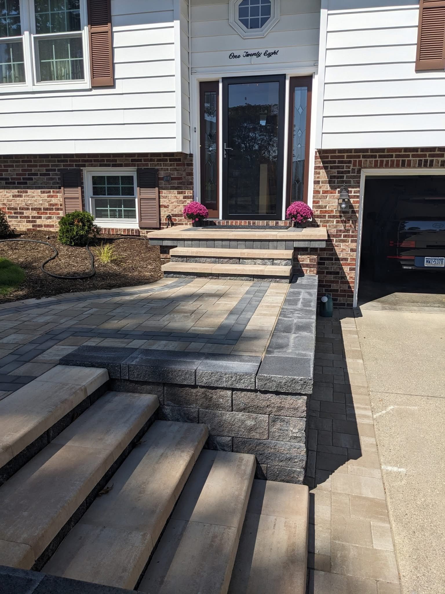 Front exterior of a house with stone steps and walkway. Brick and white siding. Flowers in pots flank the front door.
