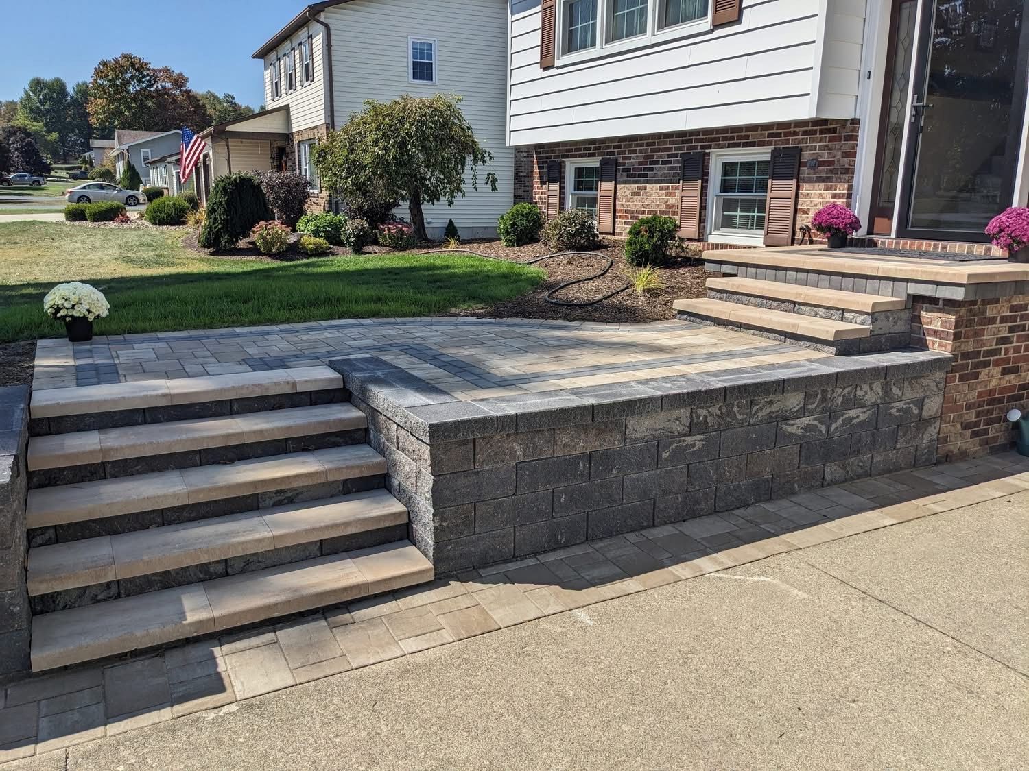 Stone steps and patio lead to a house entrance; brick and siding exterior; sunny day.