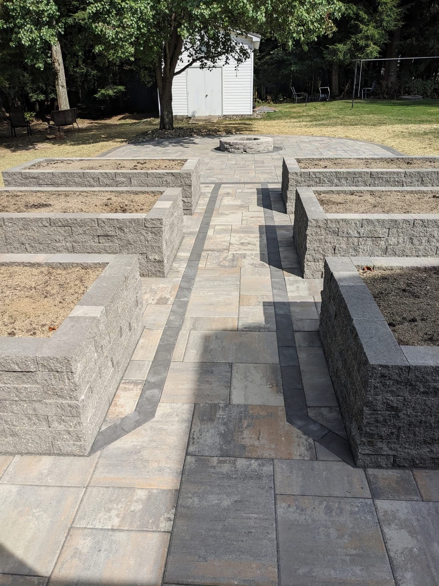 Stone patio with raised garden beds and a small white shed in the background.