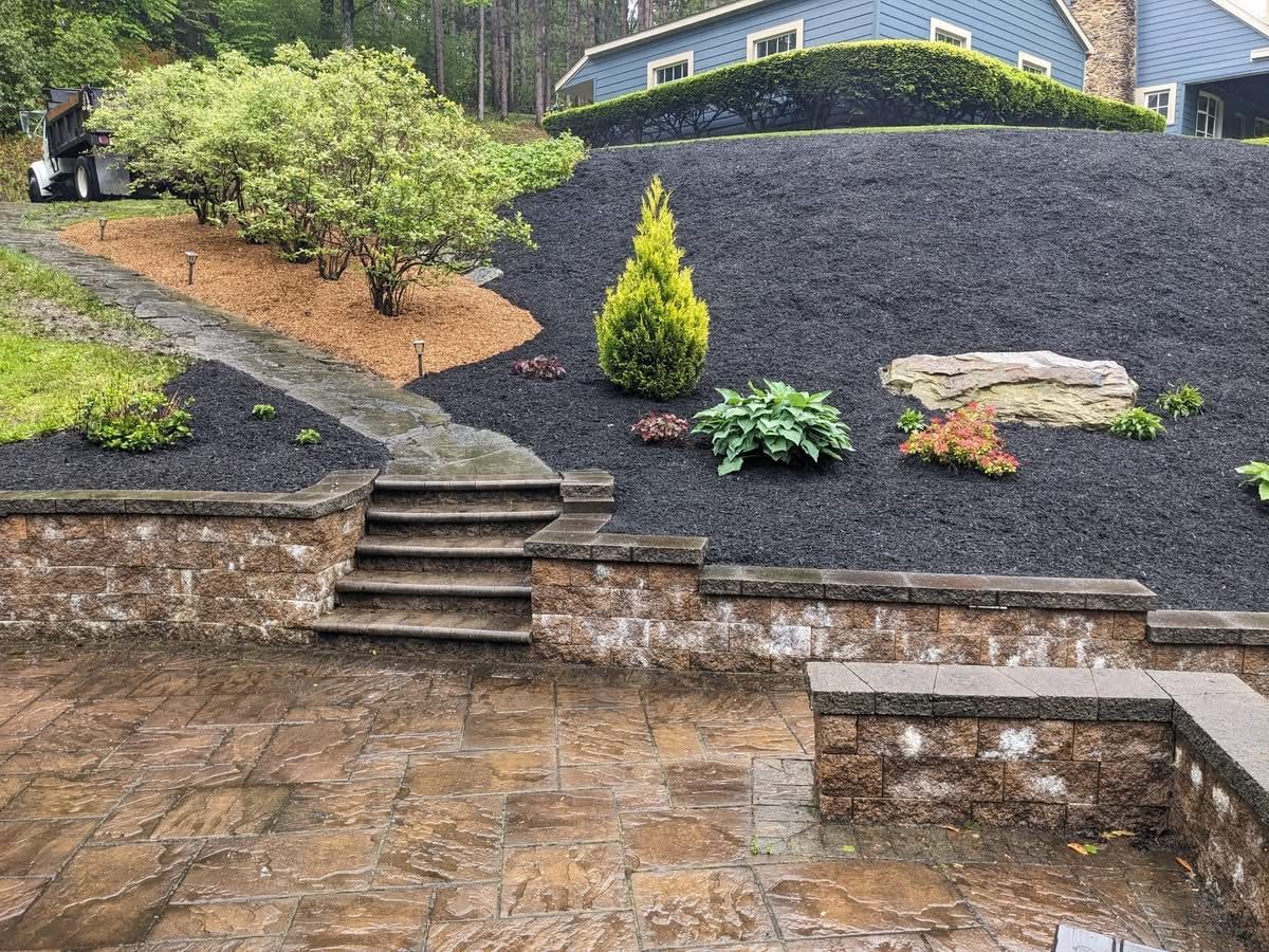 Stone patio with retaining walls and steps leading up to a mulched garden bed with various plants.
