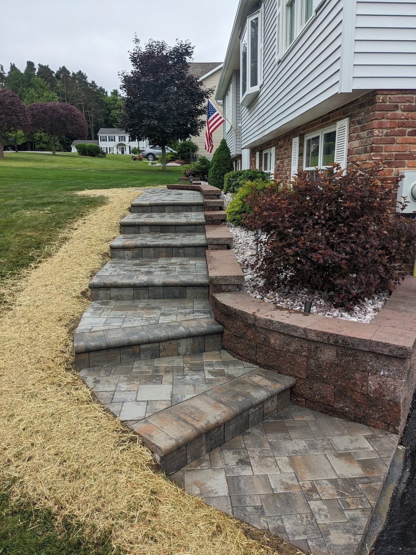 Stone steps leading up to a house with brick and siding, surrounded by grass and landscaping.