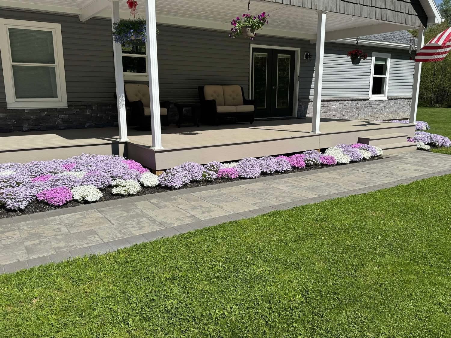 Front of a gray house with porch. Pink and white flowers border the walkway along the porch.