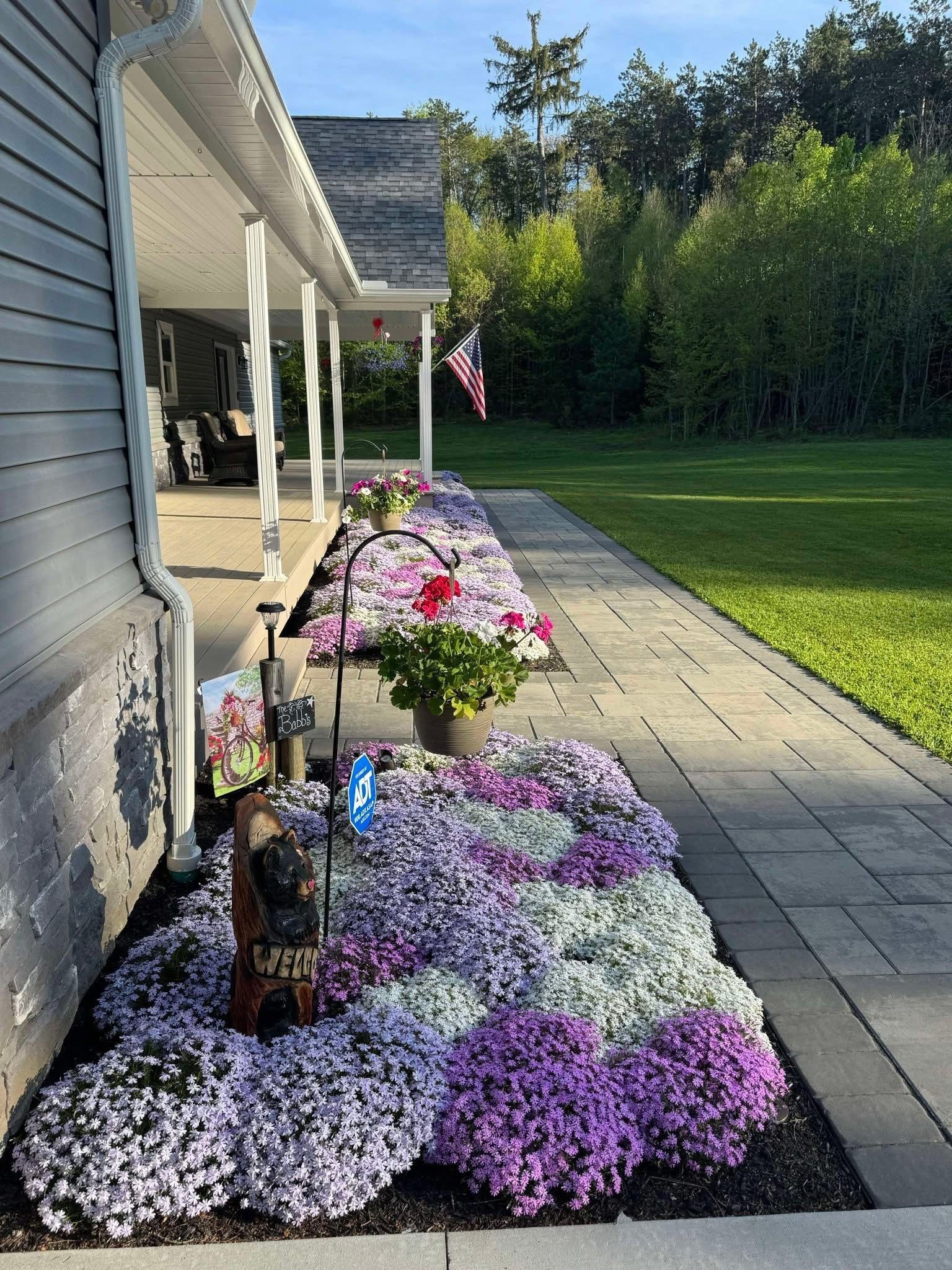 Low-angle view of a house with a row of vibrant pink, purple, and white flowers in front of the porch.