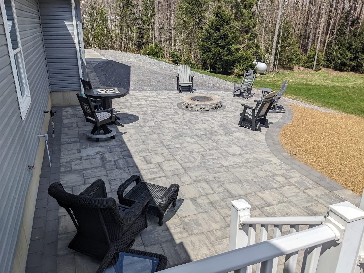 Patio with fire pit and seating, edged with gravel, beside a house and grassy area.