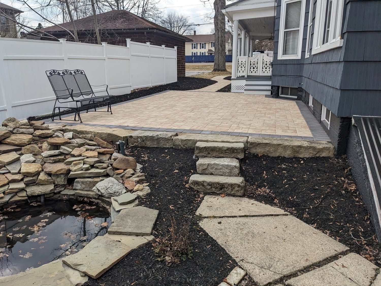 Backyard with a gravel patio, rock pond, stone steps, and a white fence.