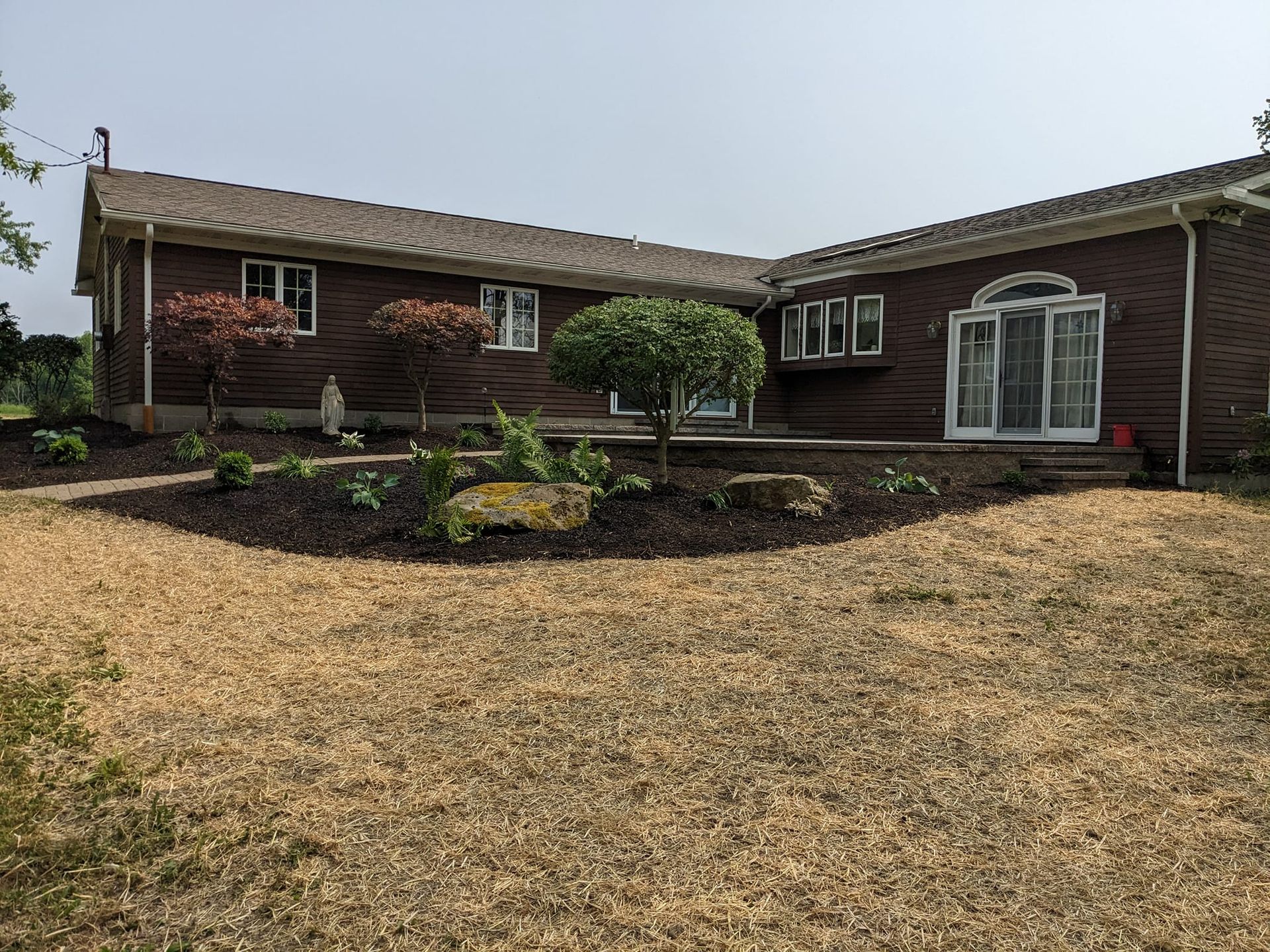 Nighttime shot of a patio with a fire pit, stone wall, and illuminated pillars. Dark trees in the background.