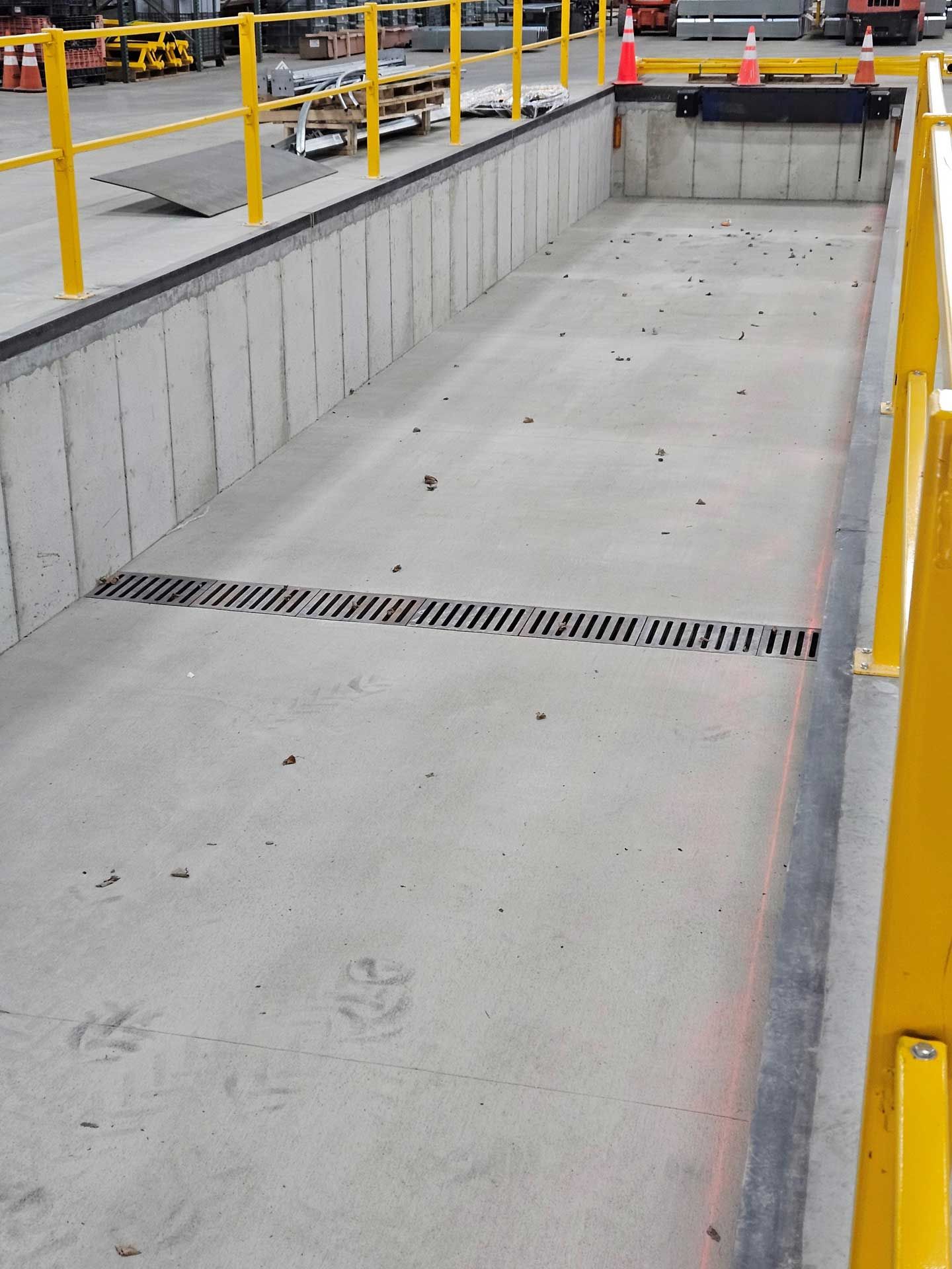 A concrete ramp with a yellow railing and a drain