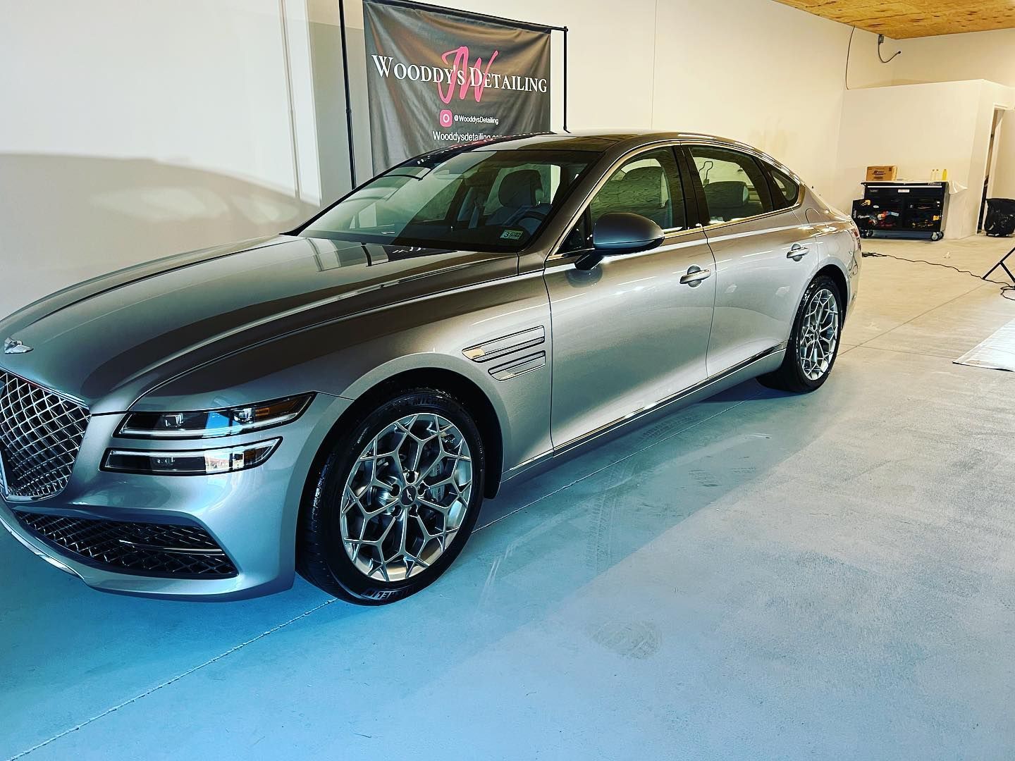 Silver Genesis G80 sedan parked in a garage with a black banner in the background.