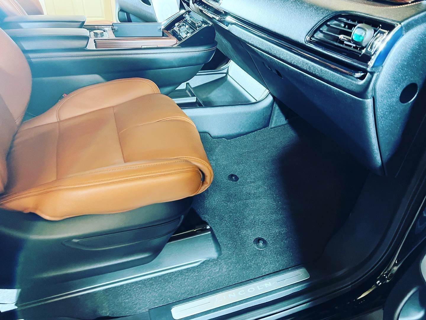 Interior view of a vehicle: brown leather seat, black dashboard, dark carpet flooring.