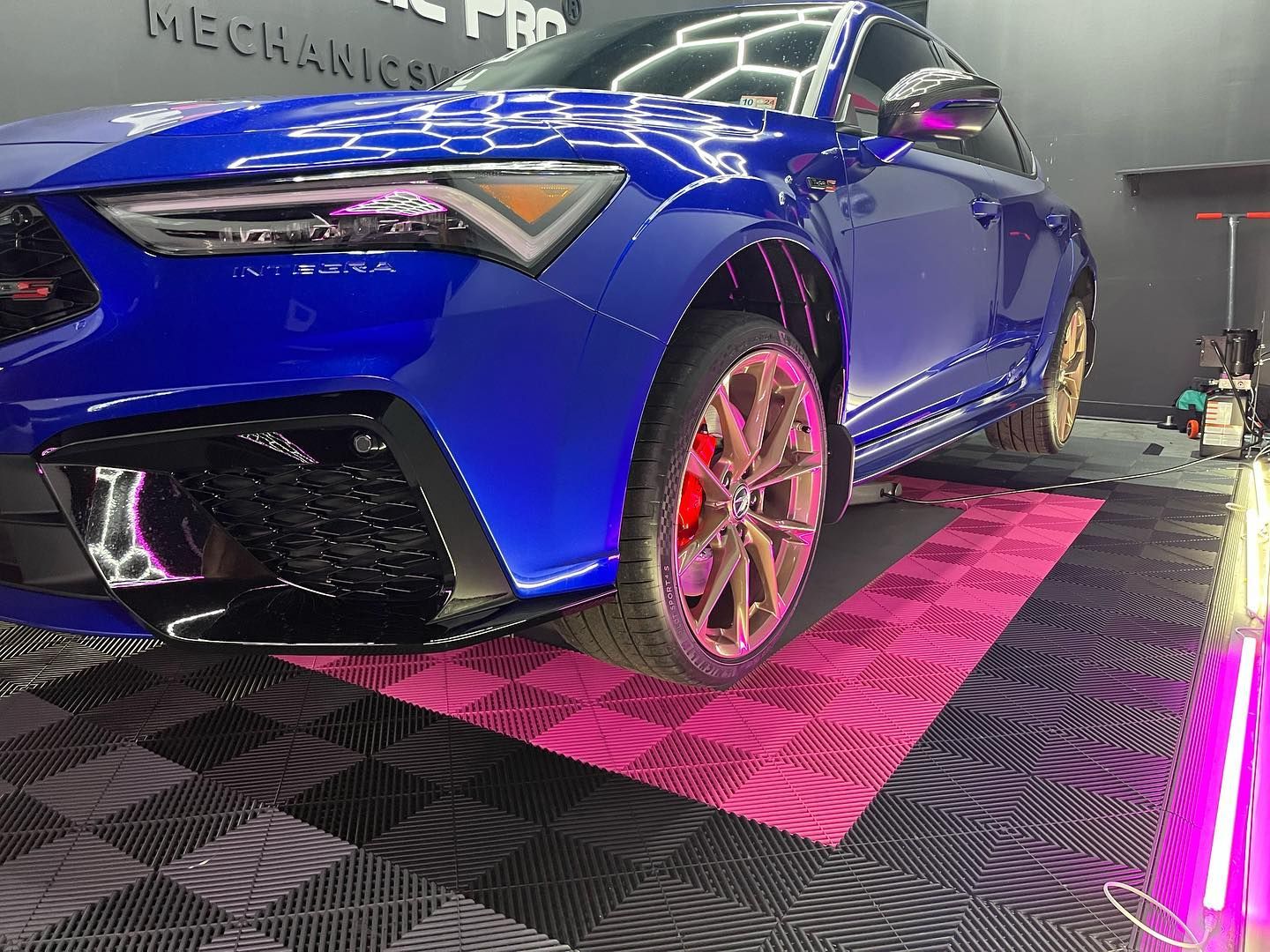 Blue car with pink wheels on a pink and black checkered floor, lit by purple lights.