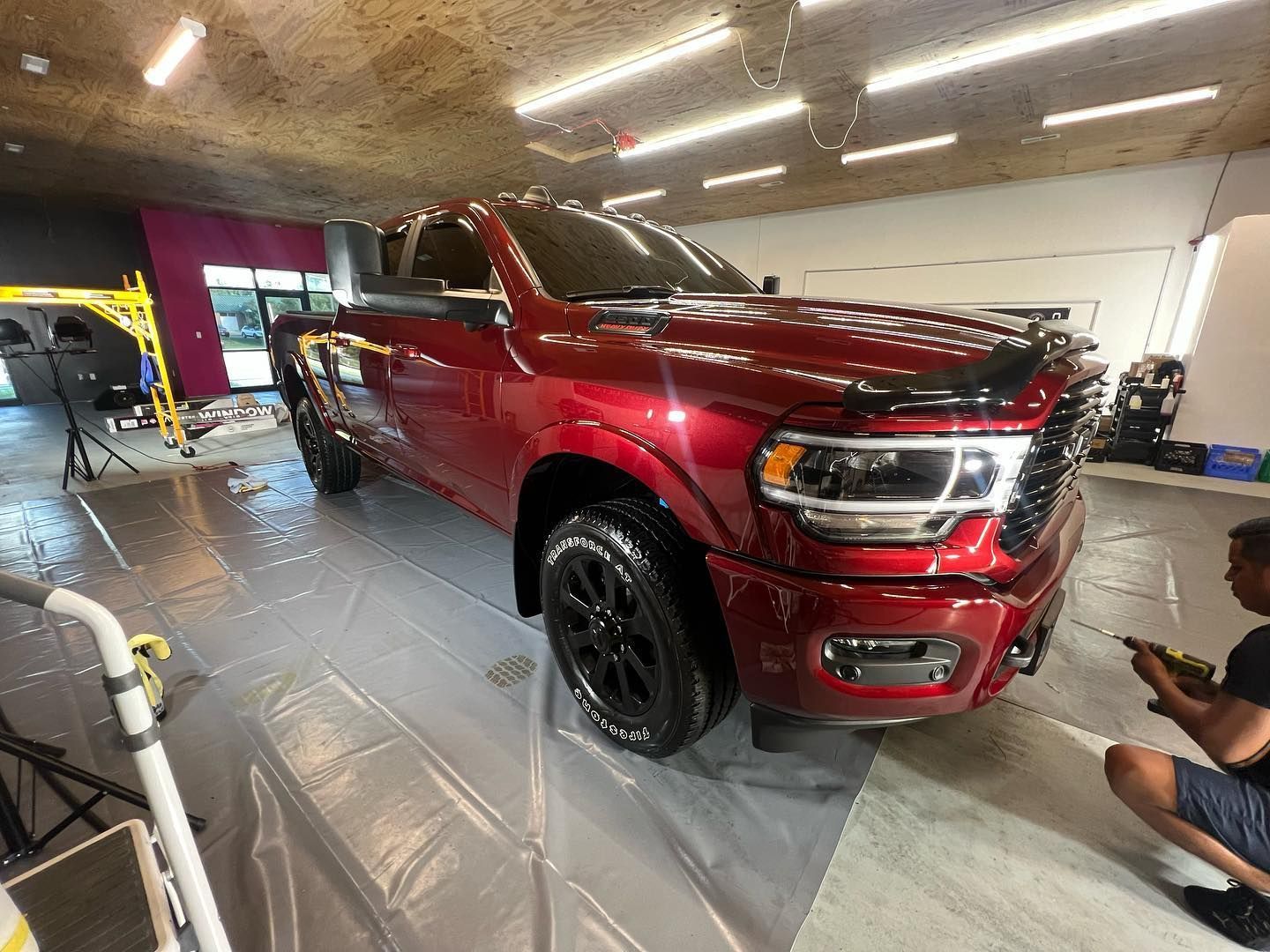 Red pickup truck inside a garage being worked on; person kneeling nearby.