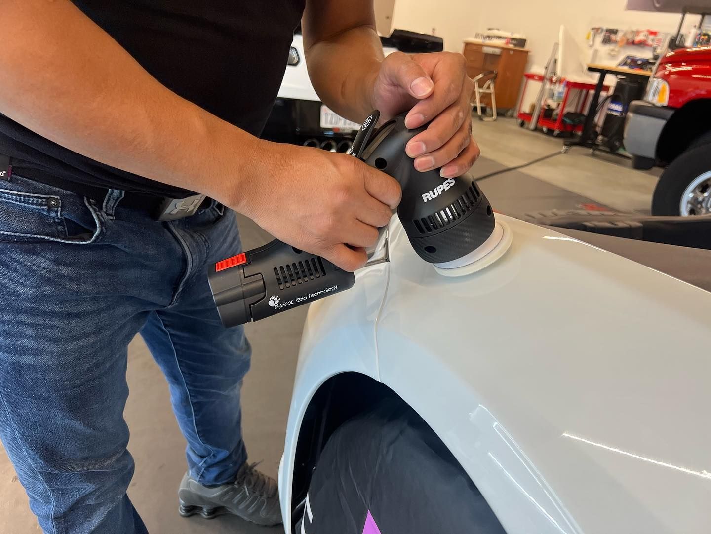 Person using a power polisher on a white car in a garage.