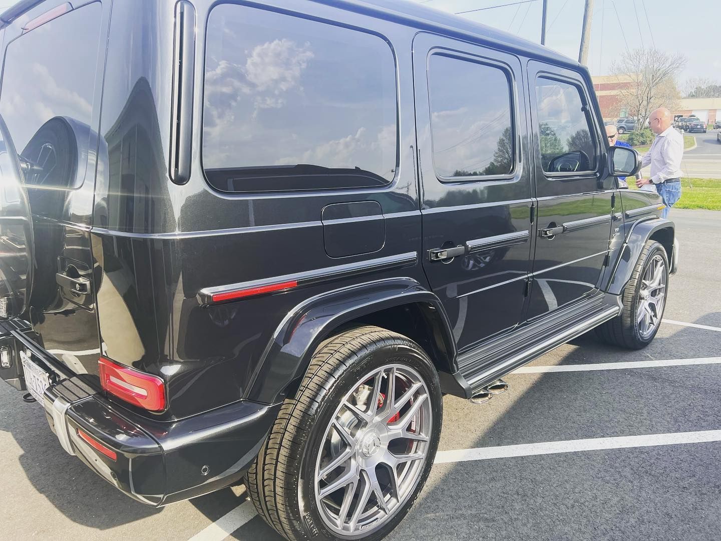 Black Mercedes-Benz G-Class SUV parked on pavement. Chrome wheels, tinted windows, and a person standing nearby.