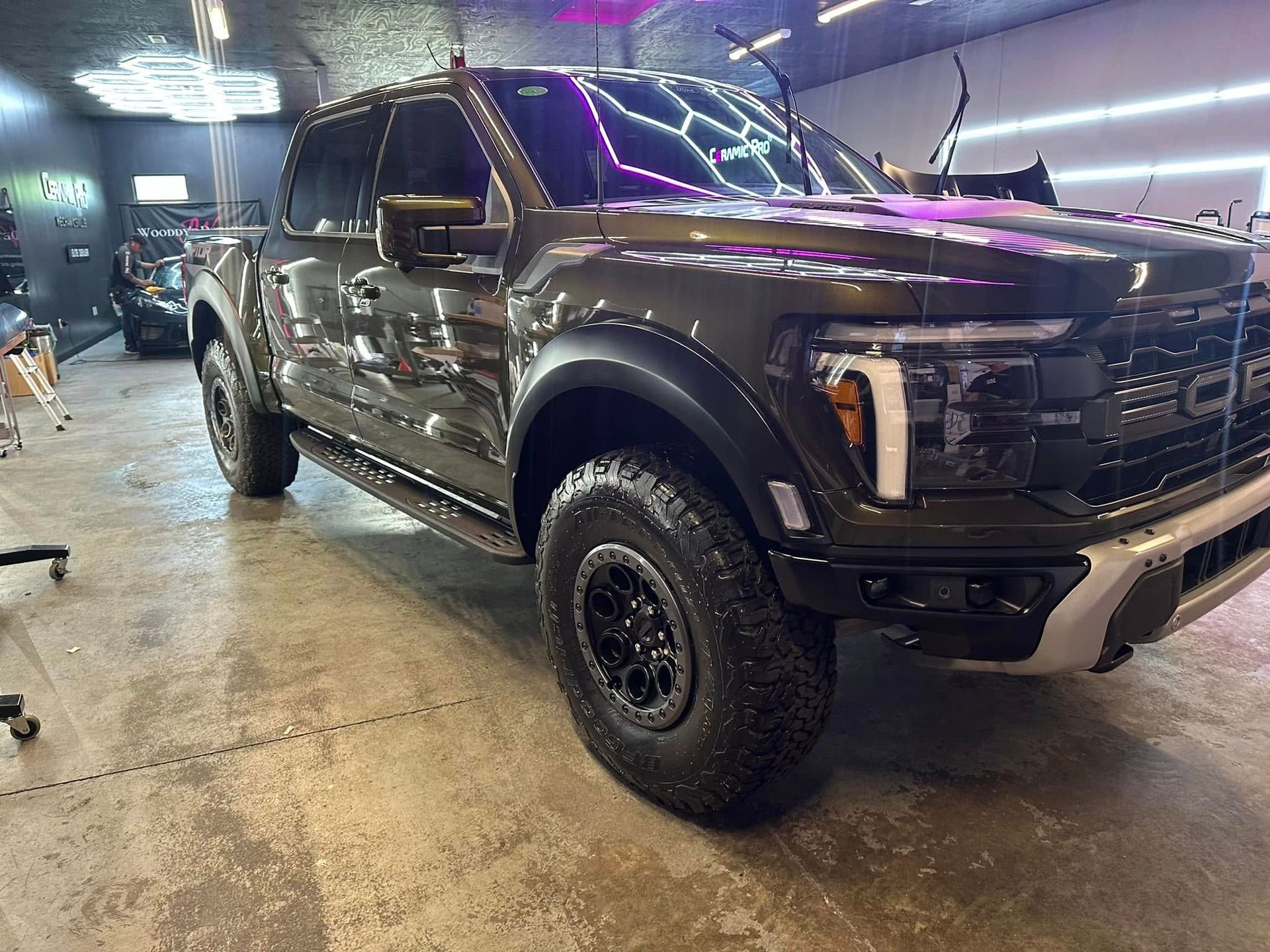 Dark-colored Ford Raptor pickup truck inside a garage with bright lights.