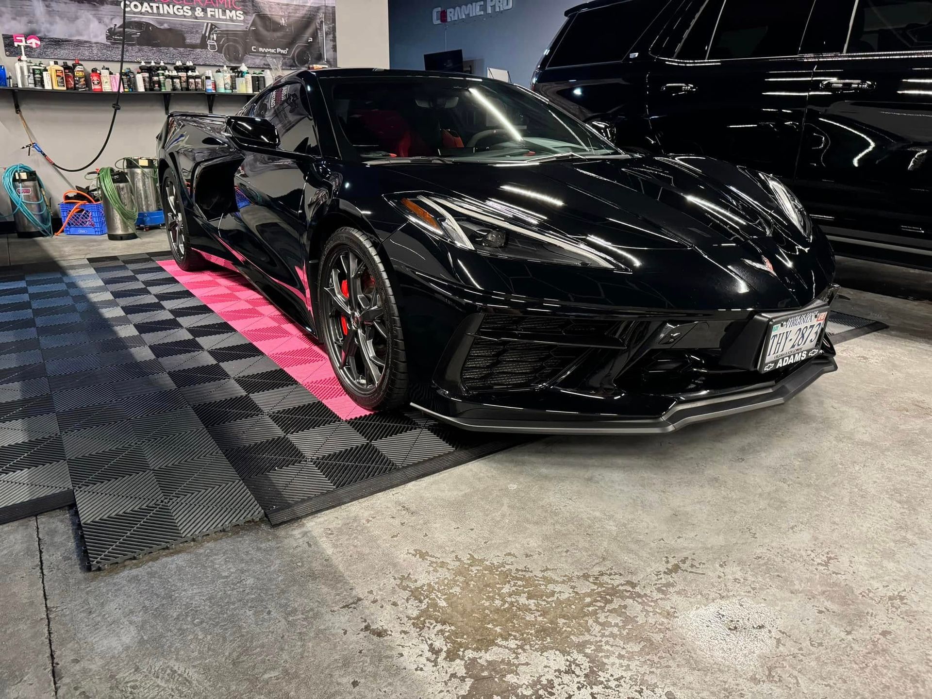 Black Corvette sports car in a garage with red interior, parked on checkered floor.