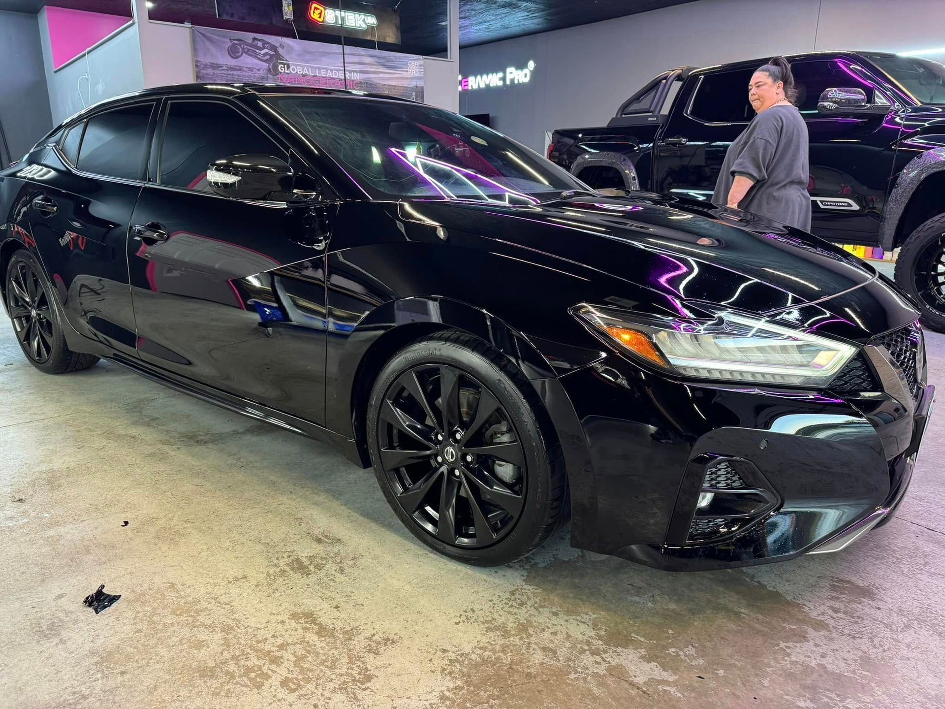 Black sedan with tinted windows, parked inside a garage. A person stands nearby.