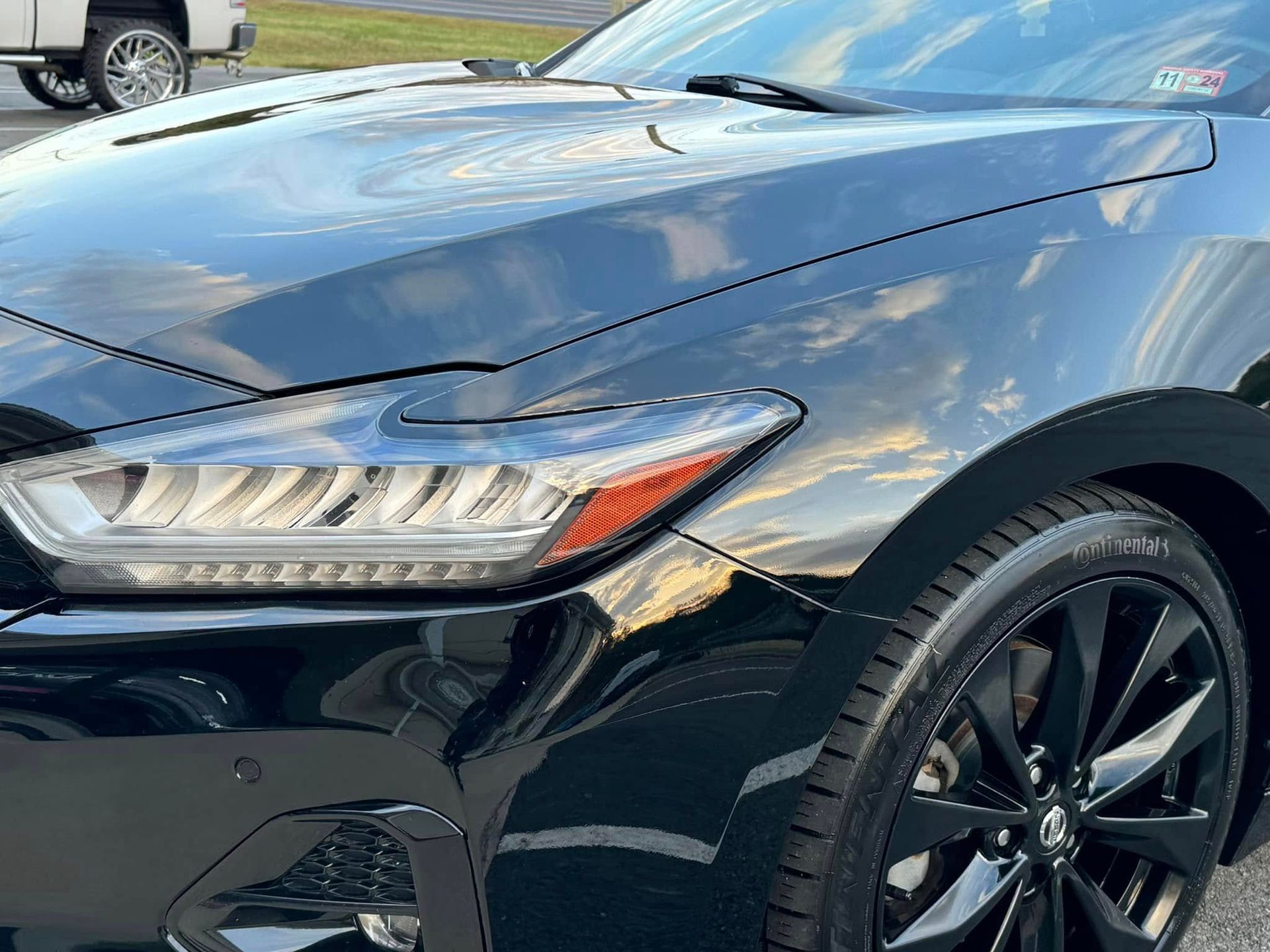 Black car's front with headlights on. Reflected sky in the hood.