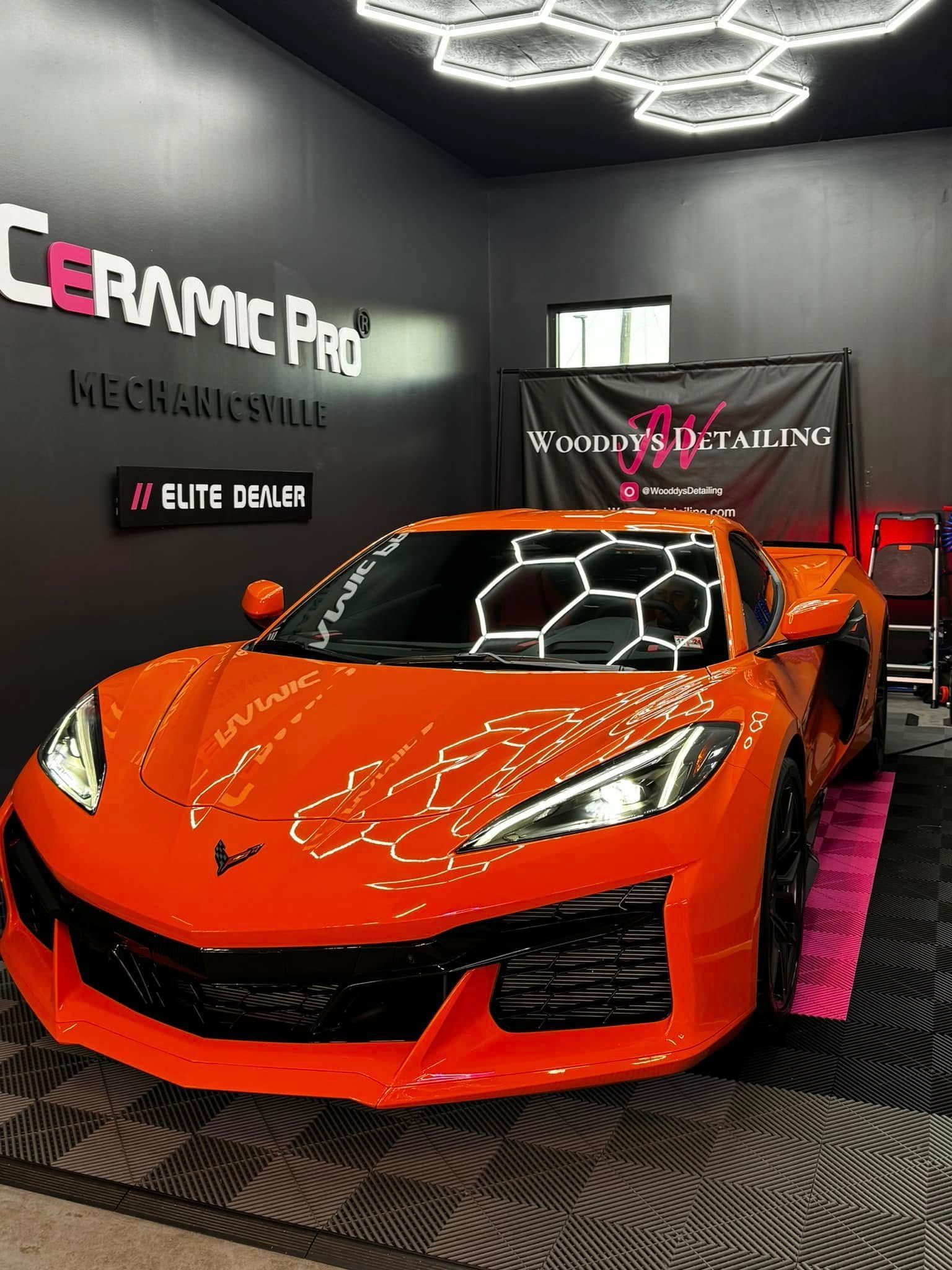 Orange sports car in a detailing shop under geometric lights with Ceramic Pro branding.