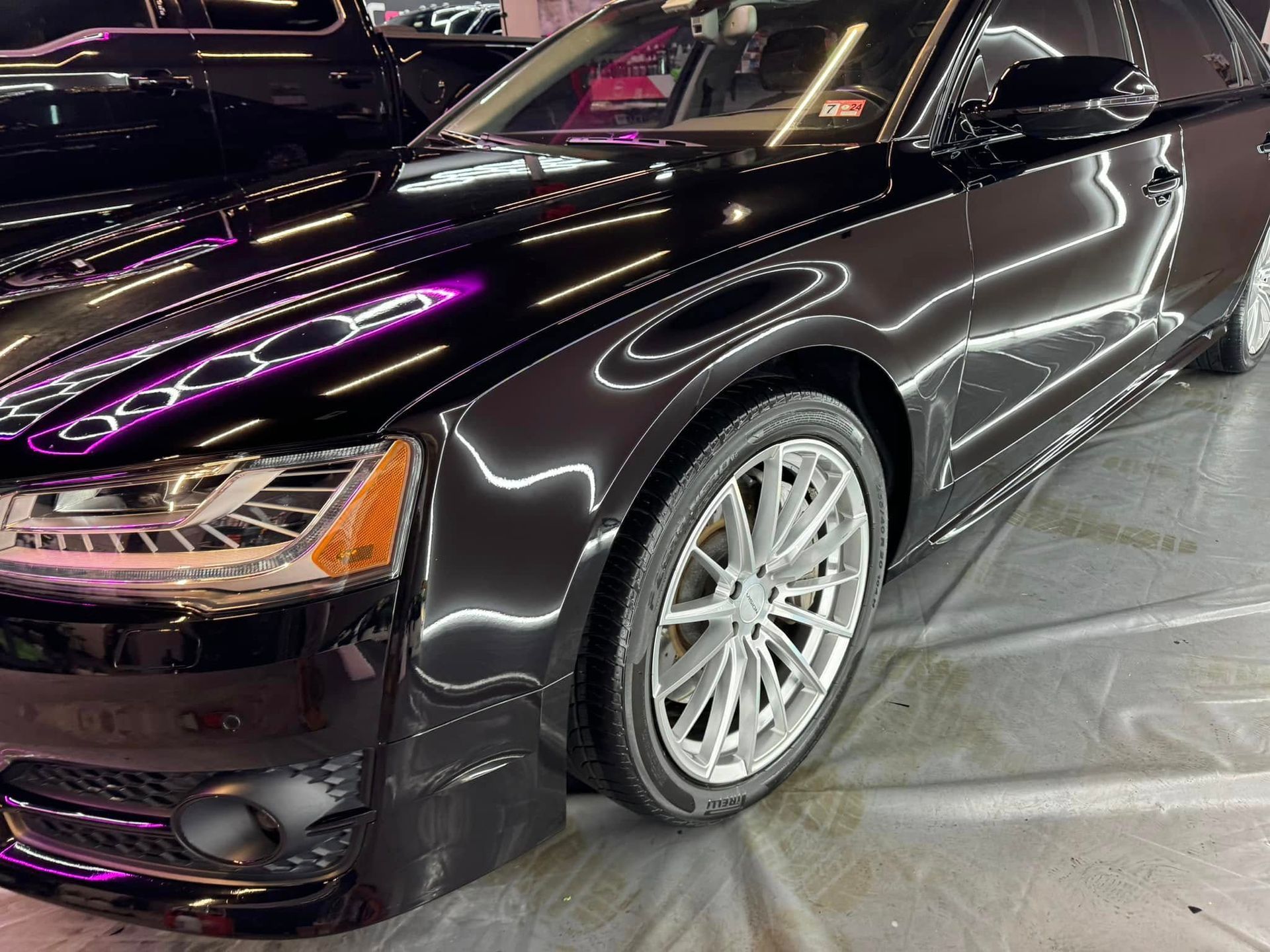 Black Audi car with silver wheels, parked indoors, reflecting bright lights.