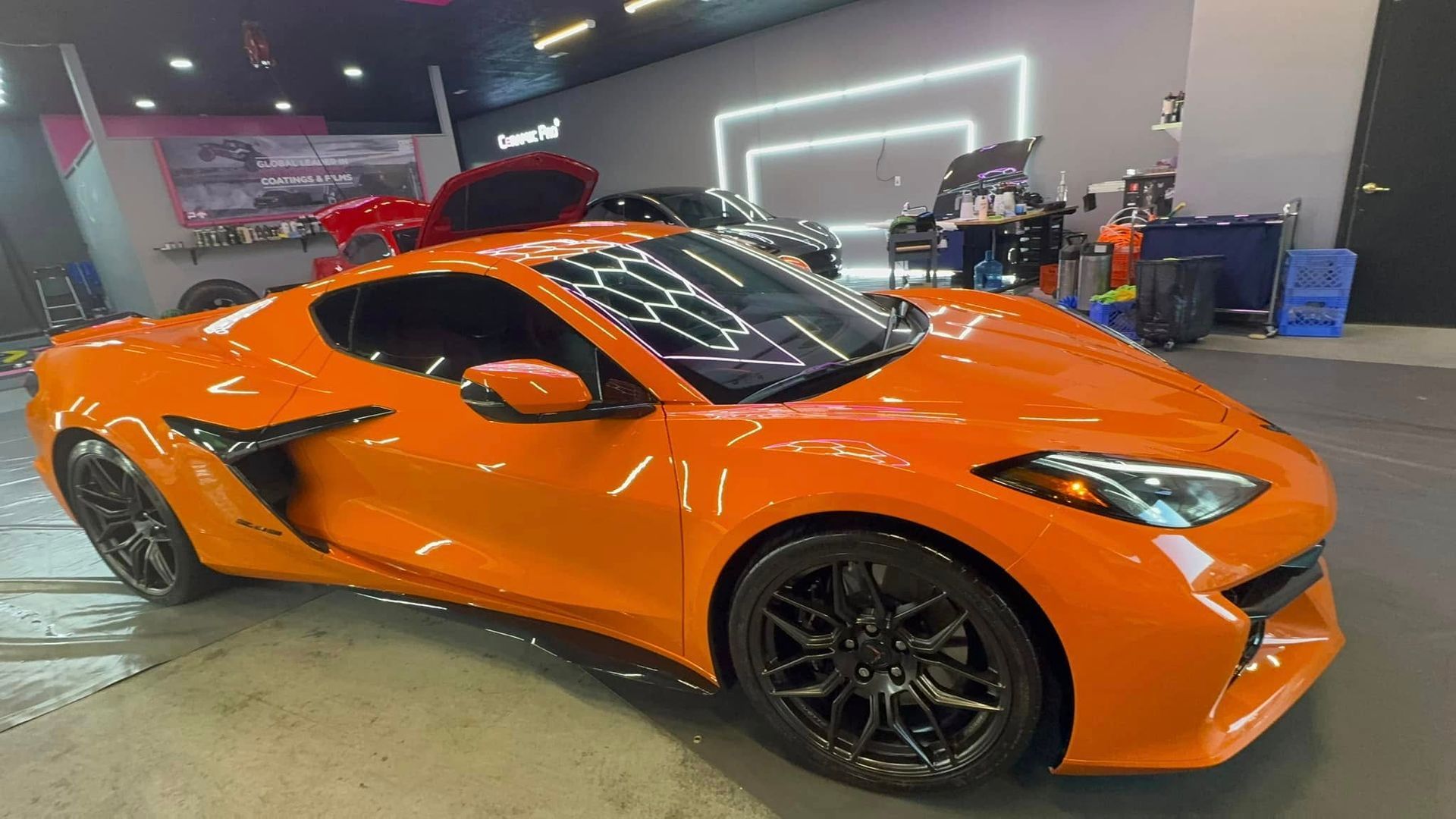 Orange sports car inside a garage with black rims, shiny paint, and bright lighting.