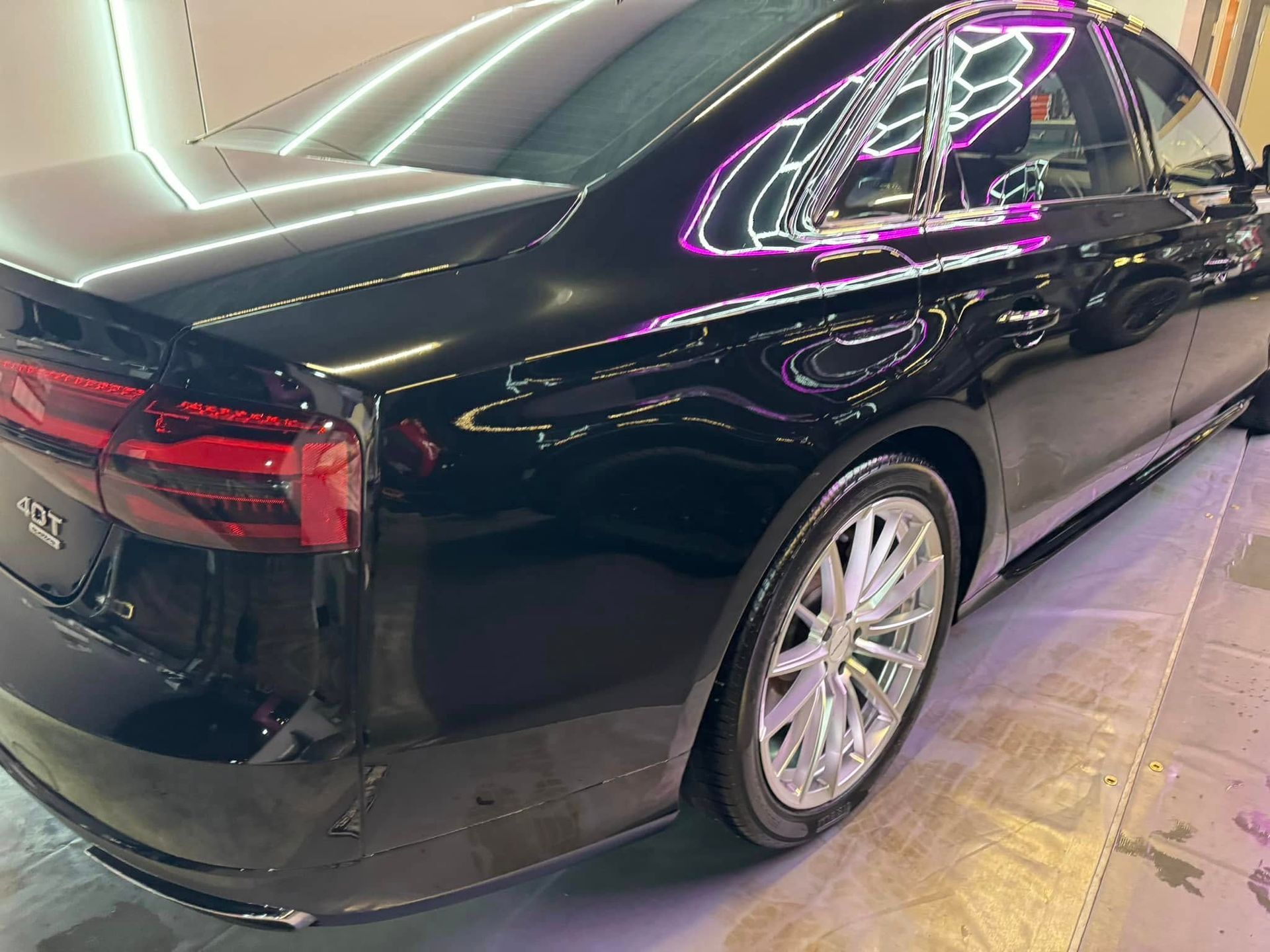 Black sedan with shiny exterior and chrome wheels, parked indoors.
