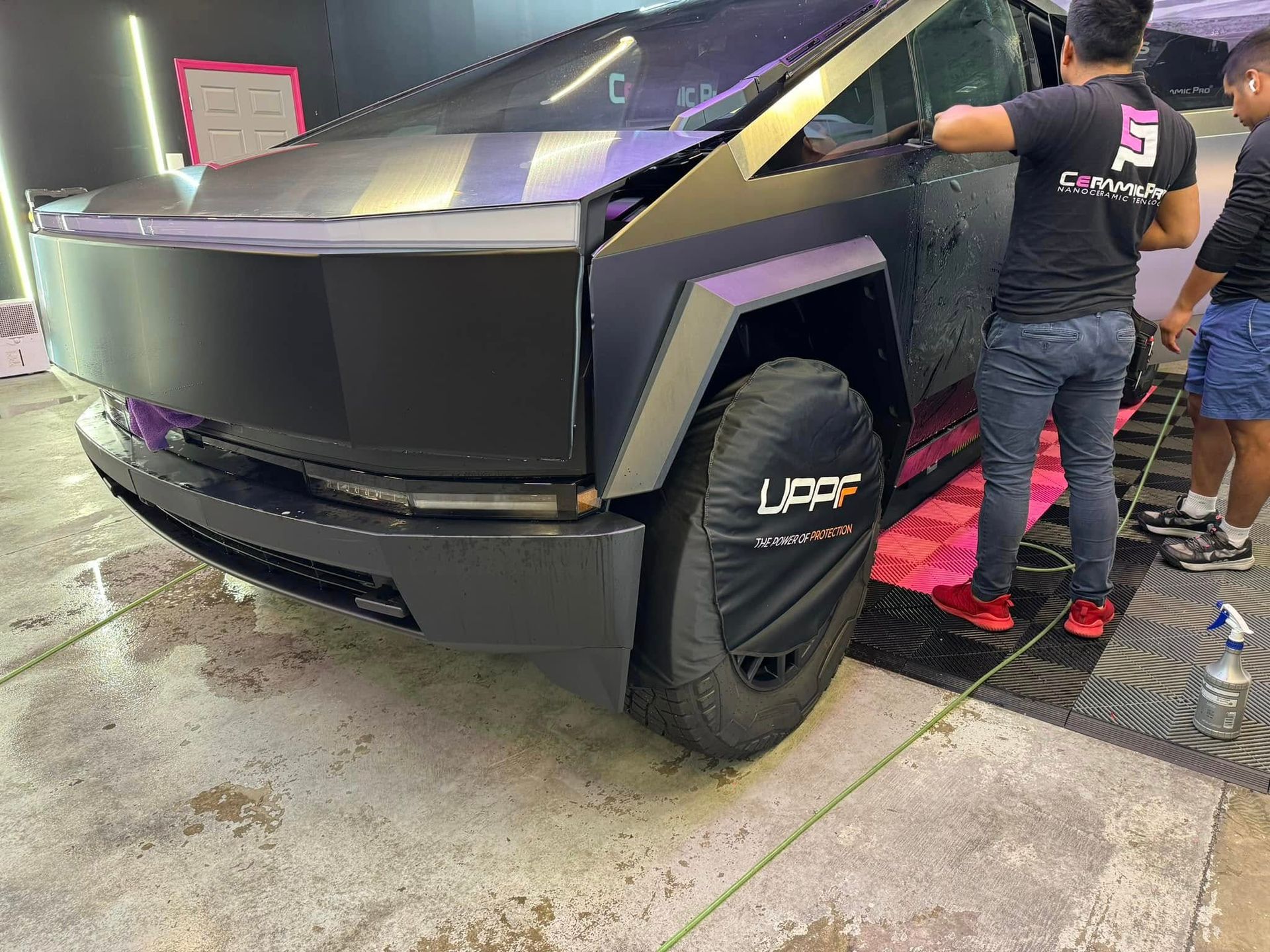 Tesla Cybertruck with a protective cover over the tire, people in a garage setting.
