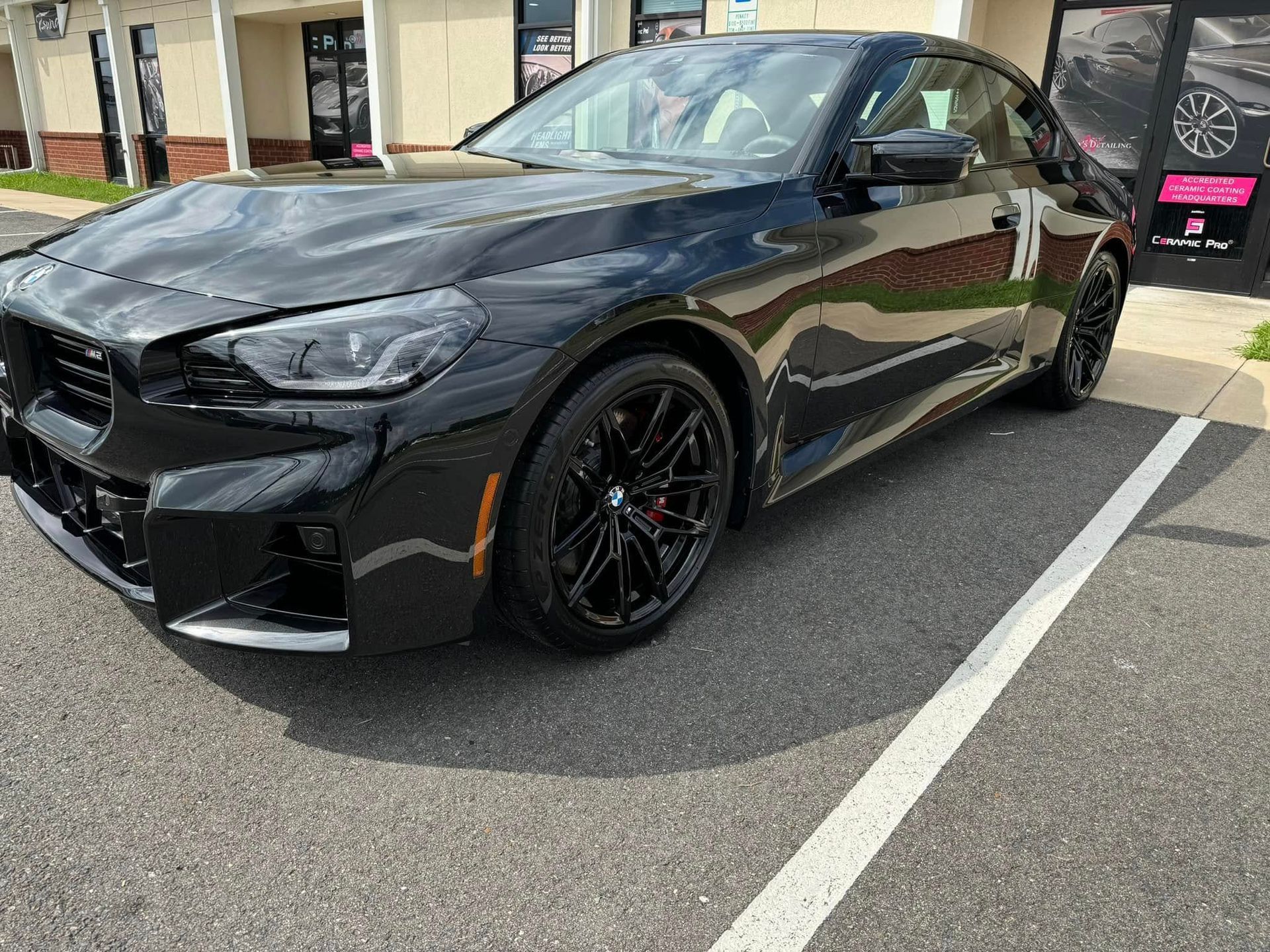 Black BMW coupe parked in front of a storefront on a sunny day.