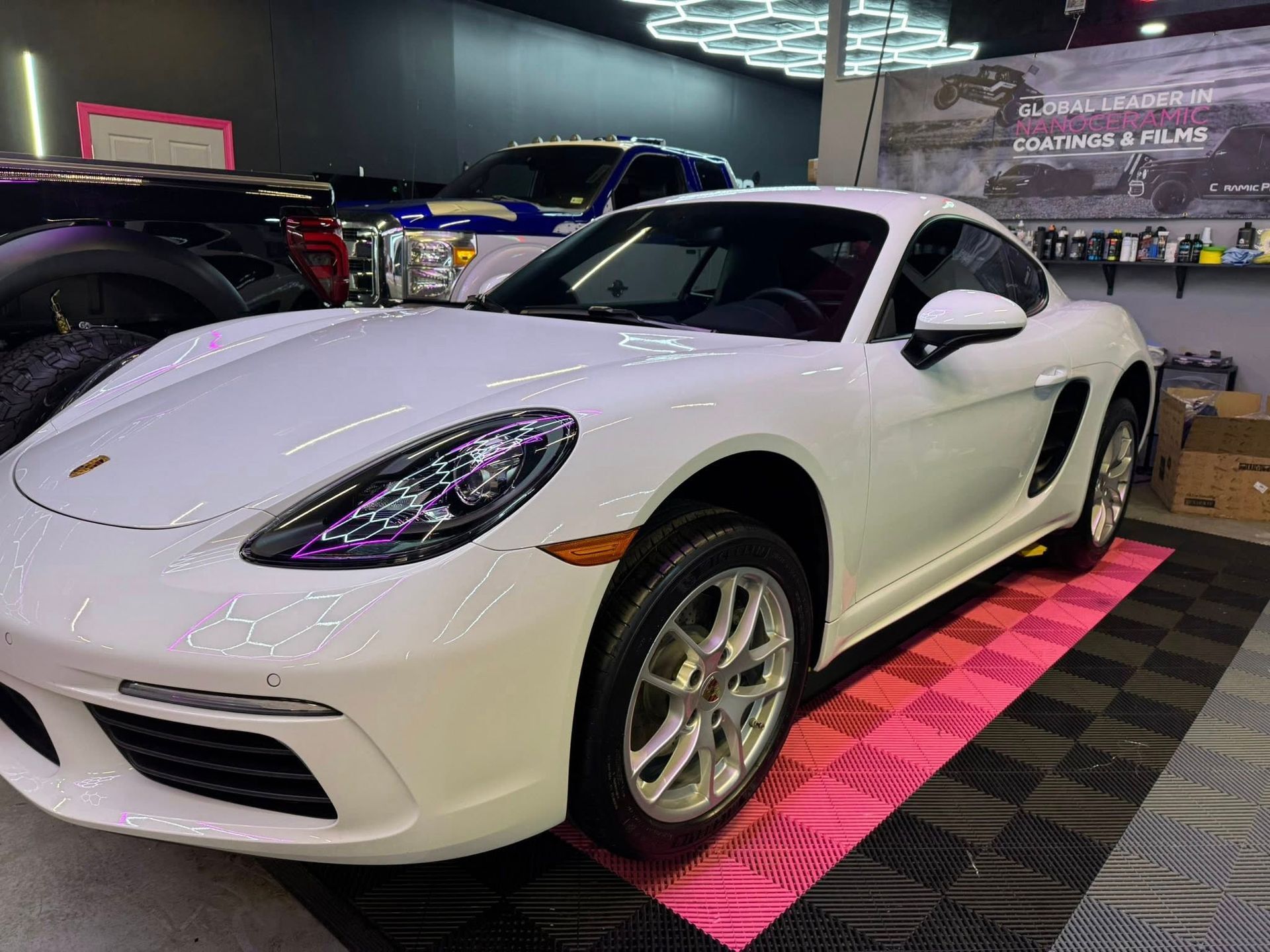 White Porsche coupe in a shop, parked on pink and black tiles.