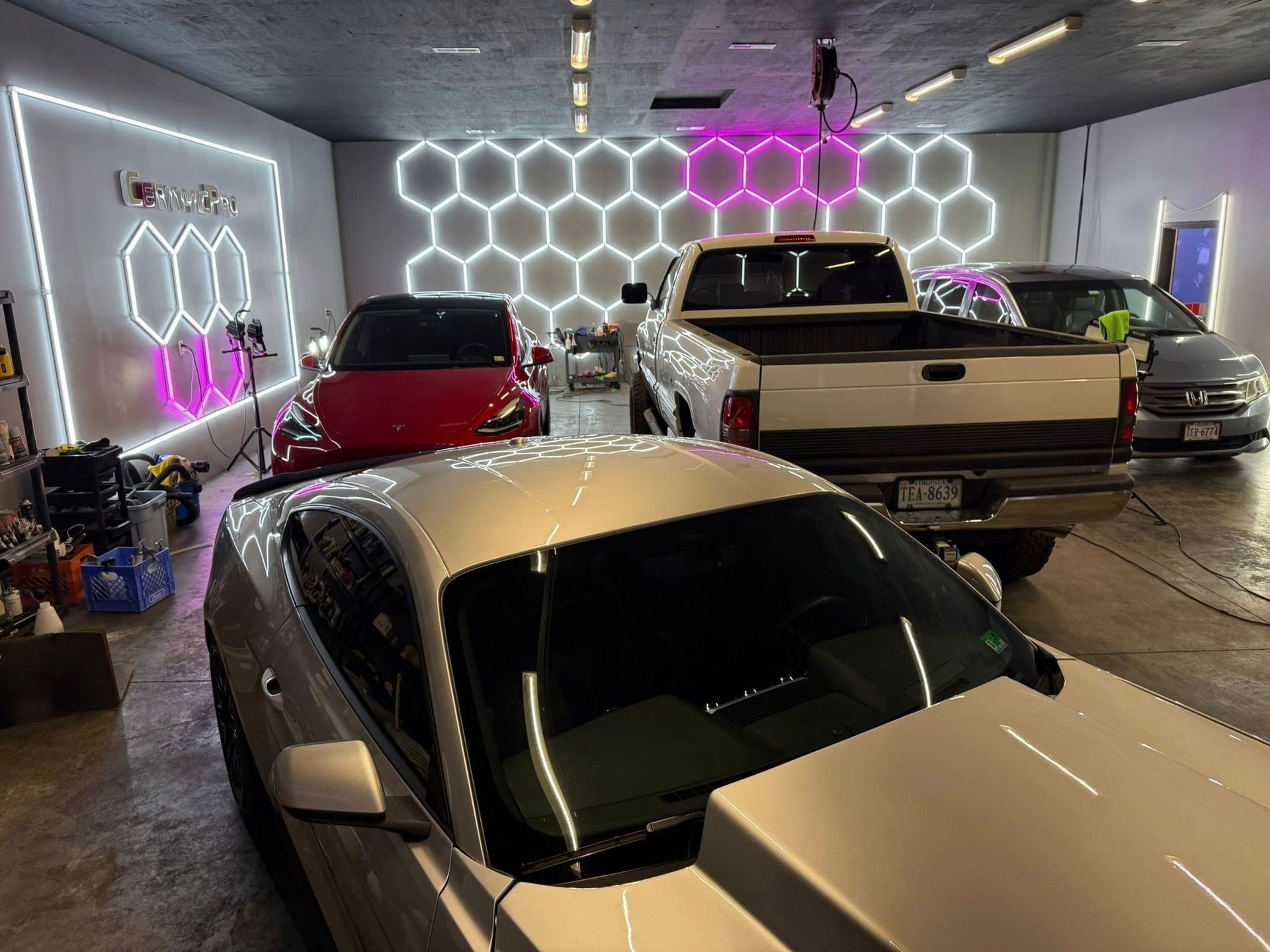 Silver car in a garage with other vehicles; honeycomb and neon lighting.