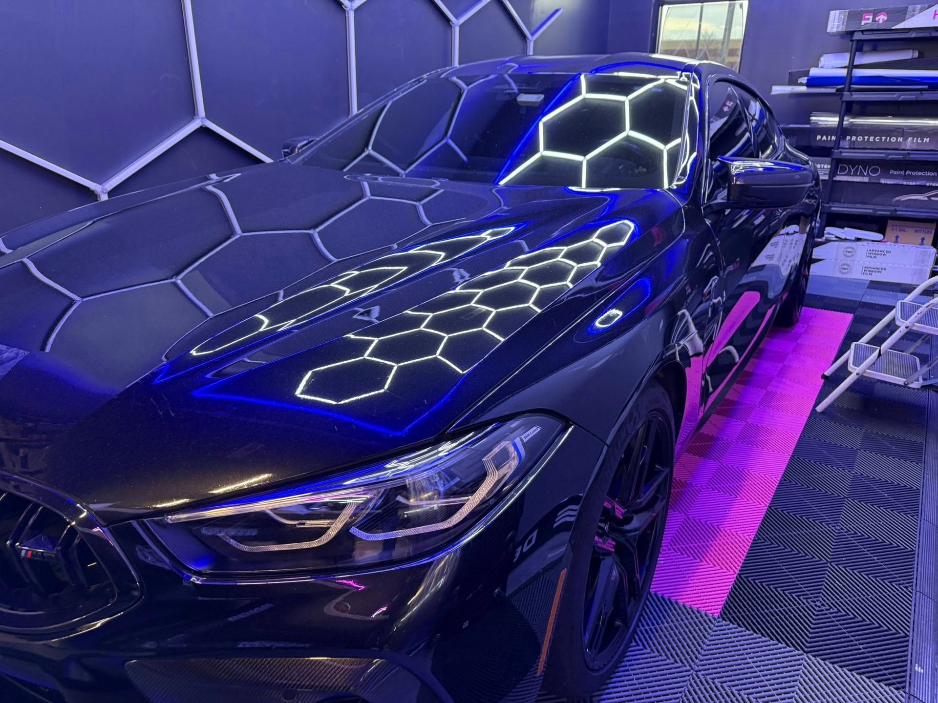 Black car reflecting a hexagonal light pattern in a shop.