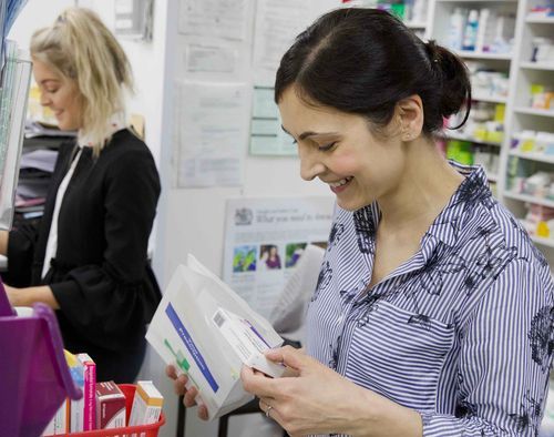 A woman is looking at a box of pills in a pharmacy.