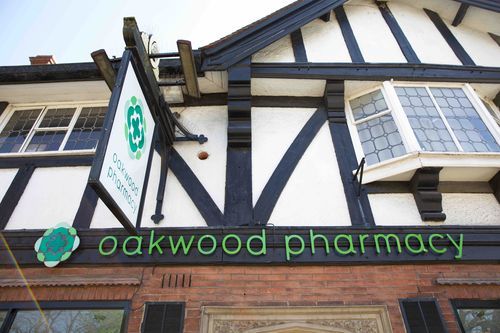 A sign for oakwood pharmacy hangs from the side of a building