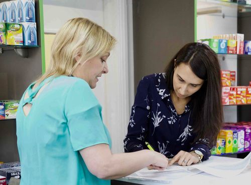 Two women are looking at a piece of paper in a pharmacy.