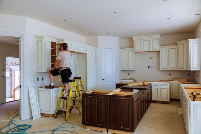 Kitchen under renovation with cabinets being installed and a person standing on a yellow ladder.