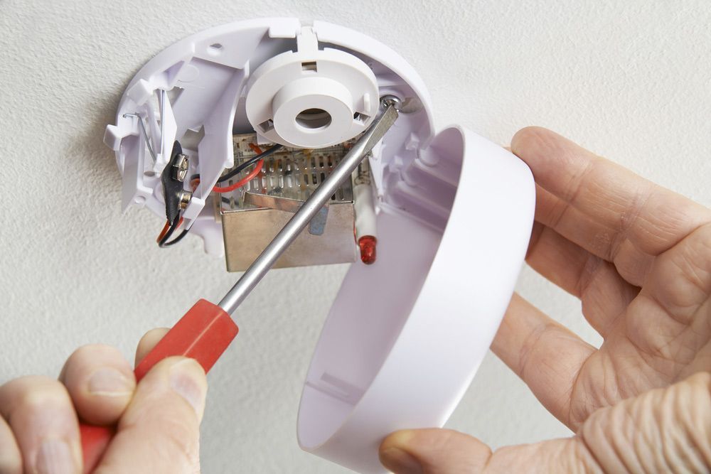 A Person is Fixing a Smoke Detector With a Screwdriver  — Anthony Cameron Electrical & Solar in Gin Gin, QLD