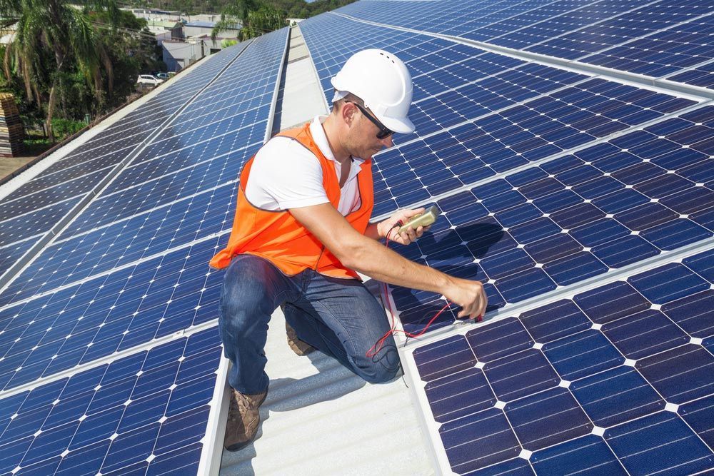Man Wearing Safety Hat Is Working On A Solar Panel On A Roof — Anthony Cameron Electrical & Solar in Kepnock, QLD