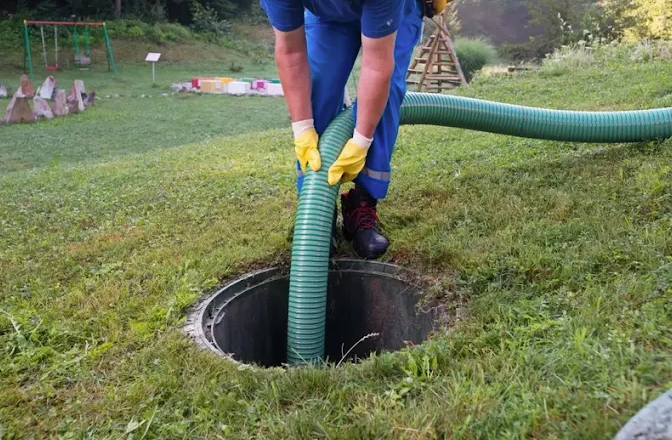A man is pumping  =a septic tank with a green ho