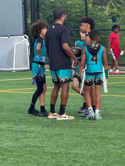 A coach and youth flag football team huddle on a green field.