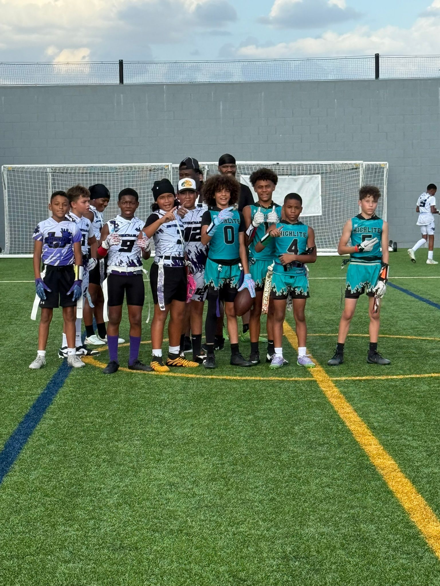 Youth flag football team poses on a field; players wear colorful jerseys, holding flags.