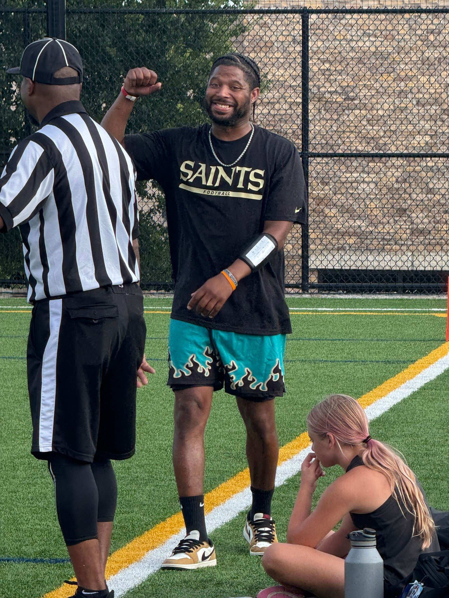 Man in Saints shirt celebrates with referee, woman watches on a field.