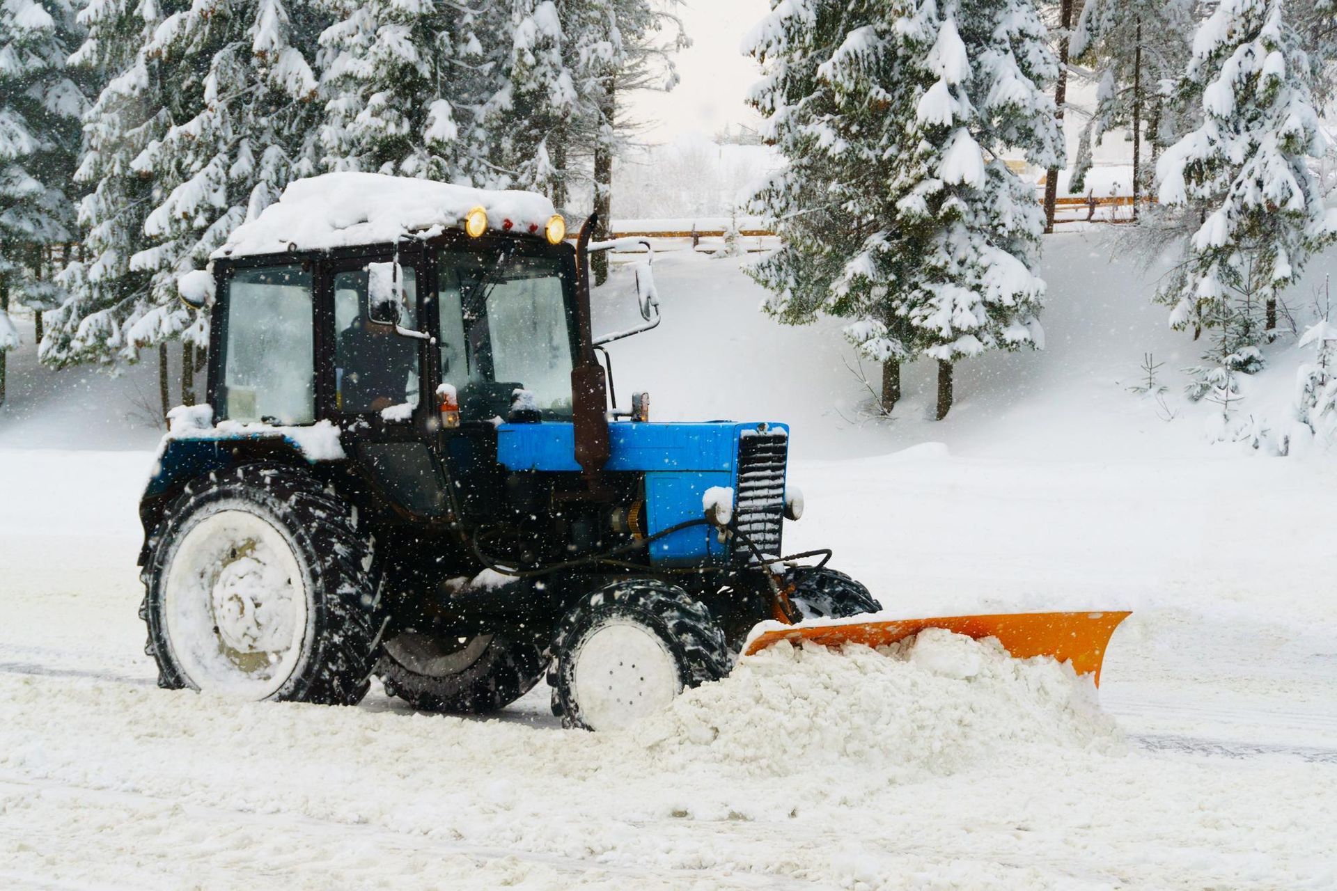 a blue and black tractor is plowing snow on a snowy road .