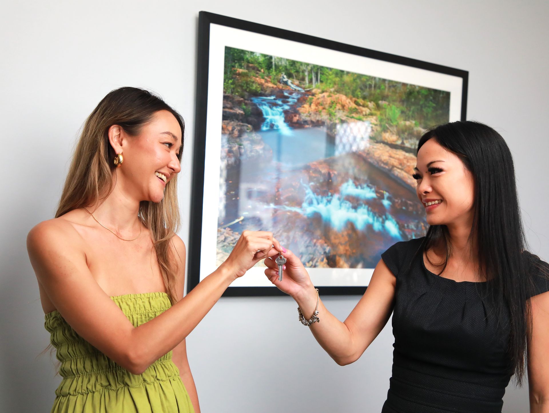 Two women are shaking hands in front of a picture on the wall.