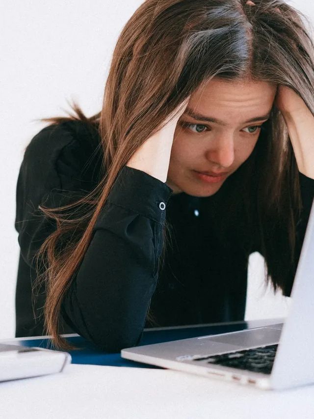 A woman is sitting at a desk looking at a laptop computer.