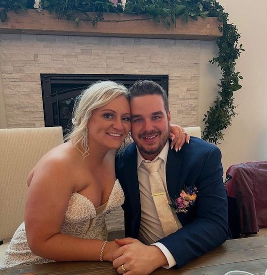 A bride and groom pose for a picture in front of a fireplace