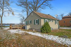 A small house is sitting on top of a snow covered field next to a body of water.